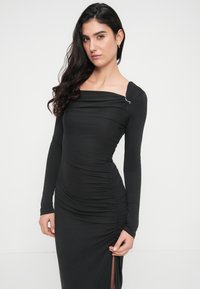 Μαύρο φόρεμα με μακριά μανίκια και ρυτιδωτό σχέδιο, τετράγωνη λαιμόκοψη και πλαϊνή σχισμή. Μεταλλική λεπτομέρεια στον ώμο προσθέτει διακόσμηση.