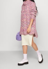 Oversized pink and purple knitted sweater with a roll neck, cream skirt with side slit, purple fluffy bag, white shoes with buckles, and patterned socks.