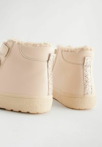 Beige faux leren enkellaarsjes met zachte bontvoering, gestructureerde rubberen zool en glinsterende accenten op de hiel en zijkant.