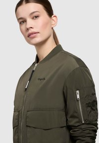 Olijfgroene bomberjack met een ritssluiting aan de voorkant, geribbelde kraag en twee voorzakken, inclusief een met rits afgesloten zak op de arm voor extra detail.