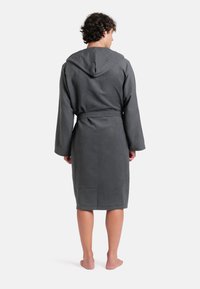 Šedý kapucínový župan vyrobený z měkkého, strukturovaného materiálu; má dlouhé rukávy, pásek v oblasti pasu a sahá do poloviny lýtek.