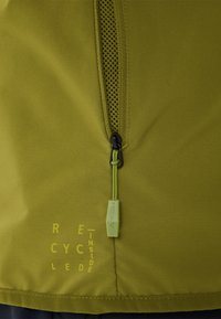 Grüner Stoff mit schwarzem Reißverschluss und Zuglasche, die mit "Vaude" beschriftet ist, gedruckter Text "Recycled Inside" unten links.