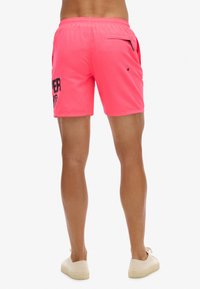 Roze zwembroek met een trekkoord in de taille, voorzien van een zijzak met rits en een zwart grafisch logo op de linkerdij.