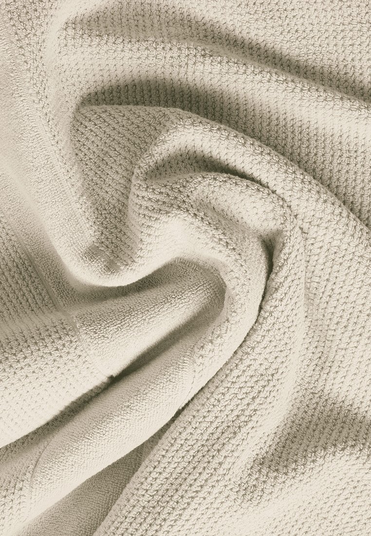 Beige strukturierte Decke mit Waffelmuster, die weichen Stoff und einen subtilen Glanz zeigt, in sanften Falten drapiert.