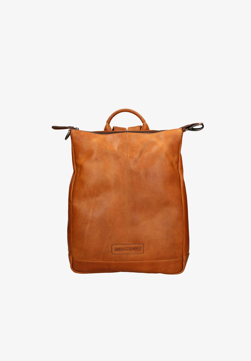 Sac à dos en cuir fauve avec poignée supérieure et fermeture éclair, design minimaliste, et patch du logo de la marque embossé sur le bas au centre avant.