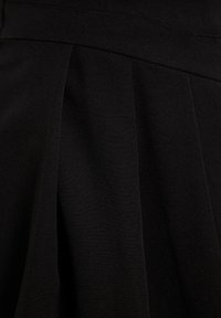 Tissu noir plissé avec des coutures visibles et des plis doux, suggérant une partie d'un vêtement ou un détail textile.