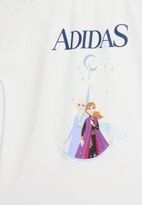 Biała koszulka z dużym niebieskim logo "ADIDAS", z nadrukiem przedstawiającym dwóch bohaterów w kolorowych strojach oraz błyskotki.
