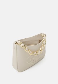 Borsa a spalla in ecopelle beige con tracolla in catena dorata, dettaglio del logo in rilievo sul fronte e tasca interna con zip.