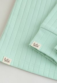 Tissu côtelé vert clair avec de petites étiquettes beiges portant l'inscription "bebe" cousues sur le poignet et l'ourlet d'un vêtement.