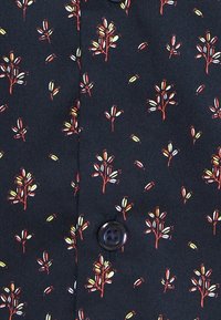 Svart tyg med ett upprepande mönster av små röda träd och gula och vita löv, med en rund svart knapp.