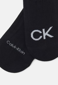 Čierne ponožky s hladkým povrchom; na stranách majú vyšívané logo šedou farbou "CK" a "Calvin Klein".