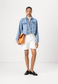 Chaqueta de denim, azul claro, diseño corto; pantalones cortos blancos, tejido texturizado; sosteniendo un bolso naranja; mocasines negros con un acabado suave.