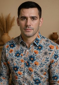 Man met kort donker haar in een knoopshirt met grijze kleur en blauw, oranje en beige bloemmotieven, tegen een beige achtergrond met vazen.