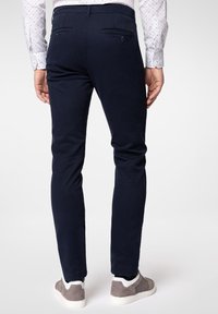 Granatowe chinosy wykonane z bawełny, o dopasowanym kroju, z tylnymi kieszeniami zapinanymi na guziki, dopełnione jasnoszarymi sneakersami.