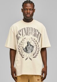 Beige oversized T-skjorte med grafisk trykk av en statue og laurbærkrans, laget av bomull med korte ermer og rund hals.