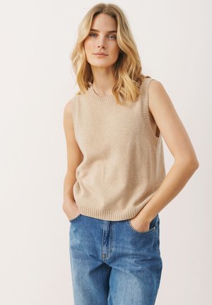 Beige pletená bezrukávová svetr s žebrovaným výstřihem a lemem, spárovaný s modrými džíny s vysokým pasem, které mají boční kapsy.