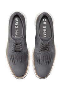 Zapatos de cuero gris con diseño perforado y cordones oscuros. Suela blanca con borde texturizado. Logotipo en la plantilla. Sin marcas visibles en el exterior.