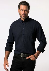 Camicia a maniche lunghe a righe blu scuro con colletto button-down, tasca frontale e maniche arrotolate. Indossata con pantaloni neri e una cintura.
