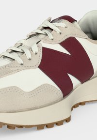 Sneaker bianca e beige con logo "N" color granato, lacci bianchi, suola texturizzata e interno imbottito visibile su sfondo semplice.