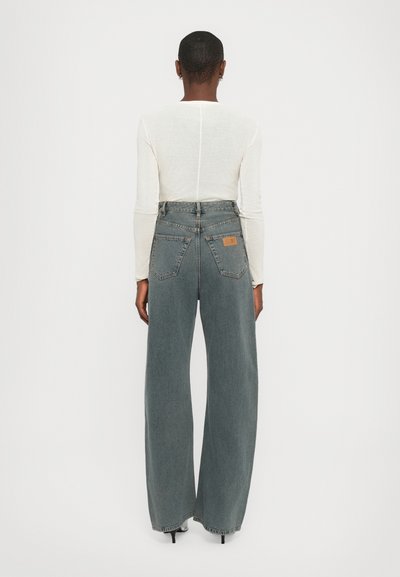 Wide-leg jeans in faded gray denim, featuring a high waist, five pockets, and a leather label on the back. Paired with a long-sleeve top.