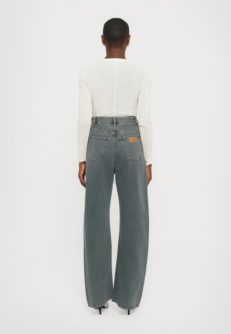 Jean large en denim gris délavé, avec une taille haute, cinq poches et une étiquette en cuir à l'arrière. Associé à un haut à manches longues.