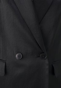 Czarna marynarka o jedwabistej fakturze, dwurzędowym zapięciu, dużych czarnych guzikach i klapach z wycięciami. Posiada boczne kieszenie i gładkie wykończenie.