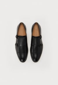 Black leather slip-on shoes with a rounded toe, featuring a smooth finish, two horizontal stitched lines, and a side buckle accent.