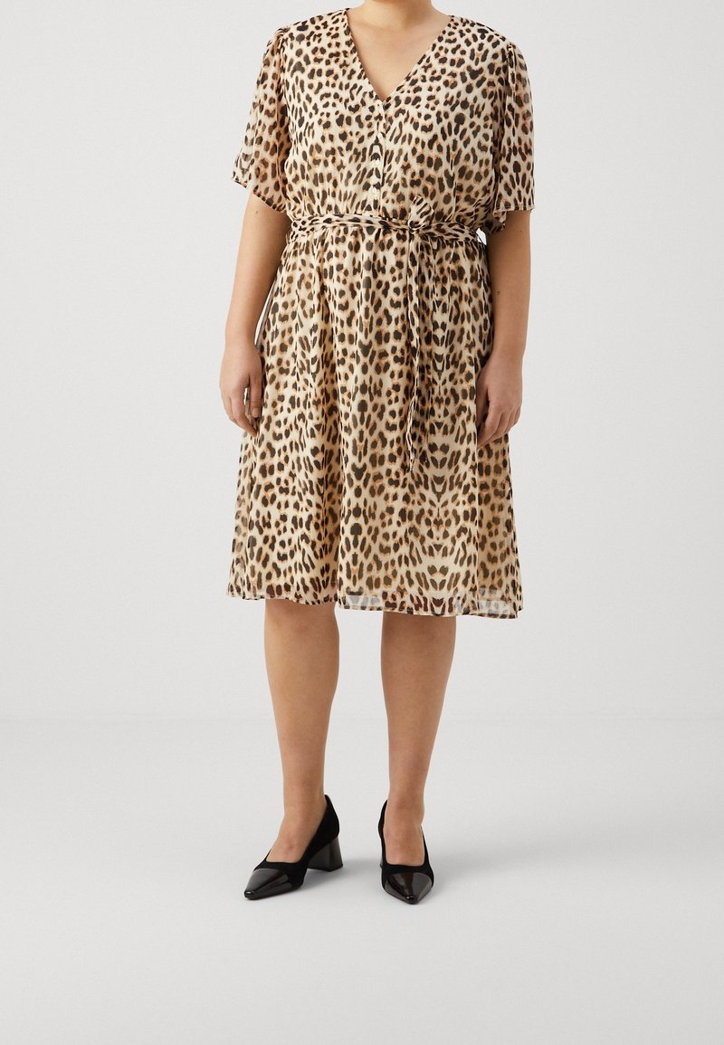 Abito a stampa leopardata con maniche corte, scollatura a V, vita cinchata e gonna fluida. Abbinato a scarpe con tacco a blocco nere.