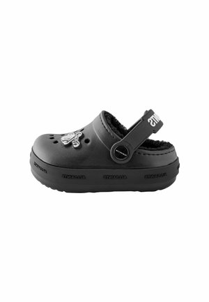 Chaussure de style sabot noire avec une doublure intérieure en fourrure, des trous de ventilation et une sangle au talon ajustable. Présente un logo en relief sur le devant.