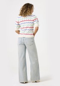 Witte trui met korte mouwen en een kleurrijk zigzagpatroon, gecombineerd met lichtblauwe wijde jeans met achterzakken en een relaxed fit.
