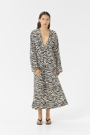 Zebra print wrap dress featuring a deep V-neck, long sleeves, and a tied waist. Made of lightweight fabric with a flowing silhouette.