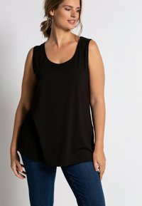 Schwarzes, ärmelloses Oberteil mit einem schmeichelhaften Rundhalsausschnitt, aus weichem Stoff gefertigt. Kombiniert mit blauen Jeans aus Denim, die einen lässigen Schnitt und eine glatte Textur aufweisen.