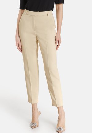 Beige tailored trousers with a straight cut, side pockets, and subtle pleats, paired with transparent heels featuring decorative accents.