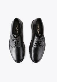 Scarpe nere in pelle con una finitura liscia, lacci e un pannello testurizzato con un emblema. Caratterizzate da una punta arrotondata e una suola resistente.