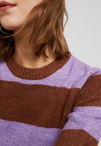 Stickad tröja med horisontella ränder i brun och lavendel, med en strukturerad yta och en ribbad halsringning.