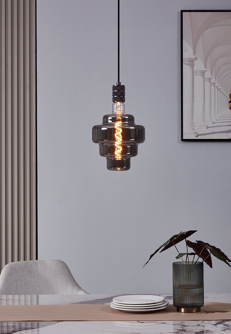 Schwarze und klare Glaspendelleuchte in Sanduhrform, ausgestattet mit einer vintage Glühlampe. Das Kabel ist schwarz und hängt über einem Tischgedeck.