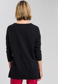Pull noir ample avec des manches longues, épaules tombantes et un col rond ; texture douce ; ourlet arrière plus long pour une meilleure couverture.