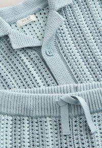 Light blue knit cardigan with a textured pattern, buttoned front, collar, and matching ribbed waistband with tied drawstring.