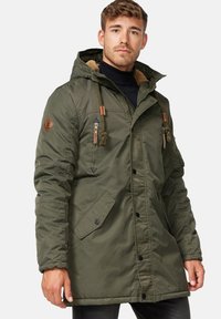 Olivgrüne, gepolsterte Parka-Jacke mit einer Kapuze aus Kunstfell, mehreren mit Reißverschluss versehenen Taschen und Zugbändern mit Kordelstoppern. Mit Lederakzenten.