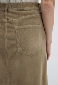 Corduroy skirt in an olive green hue, featuring a back pocket with a pointed flap, vertical ribbed texture, and a high waist design.