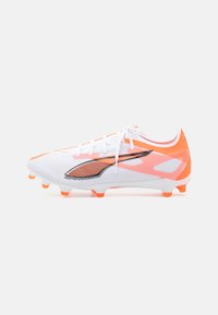 White soccer cleat with orange accents, featuring a textured surface, laces, and a distinctive black logo design. Studded outsole for traction.