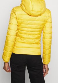 Gul pufferjakke med hætte, der har et quiltet design, elastiske manchetter og en tætsiddende talje, lavet af skinnende, glat stof.