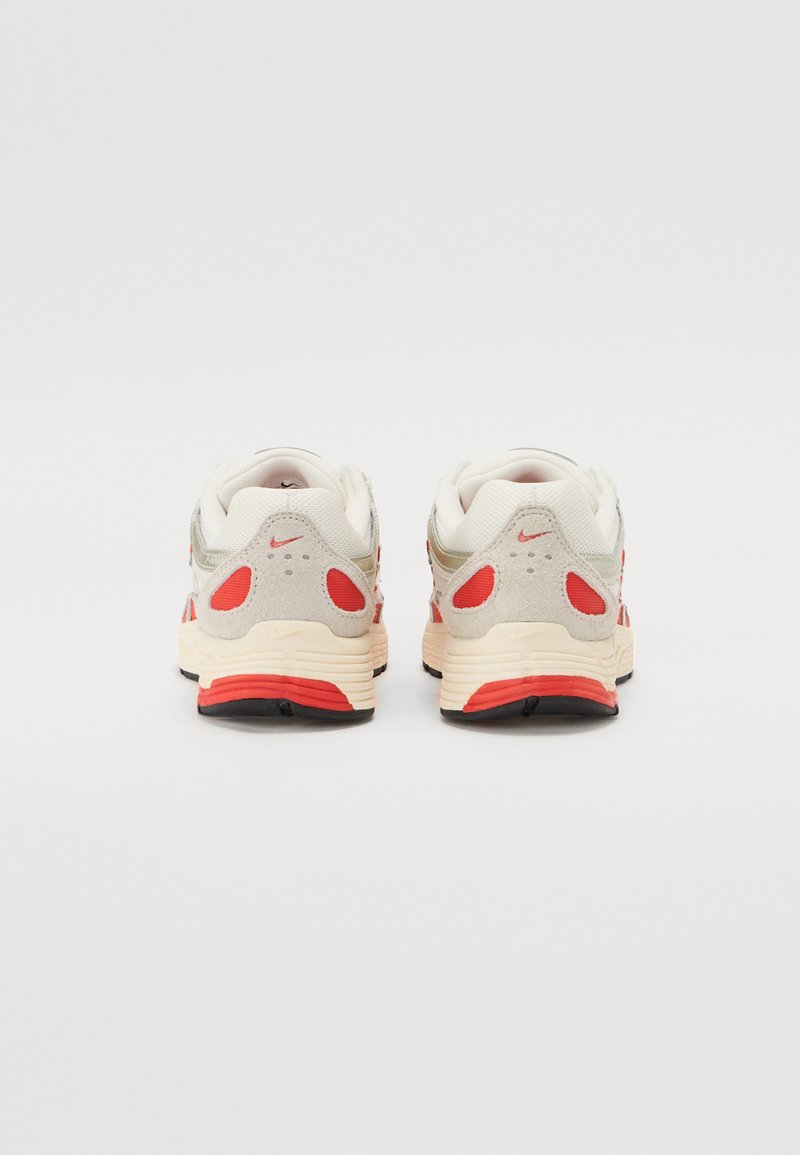 Ansicht von hinten auf beige Sneakers mit grauen Akzenten und roten Details. Glattes Material, gepolsterter Schaft und strukturierte Sohle mit schwarzen Gummibereichen.