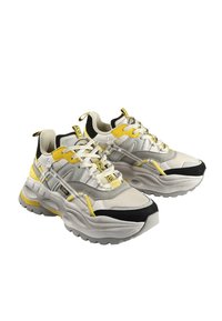 Masivne superge v beli, sivi in črni barvi z rumenimi akcenti. Iz mrežaste in semiš materialov, zaobljenim prstom, debelim gumijastim podplatom in izrazitimi vezalkami.