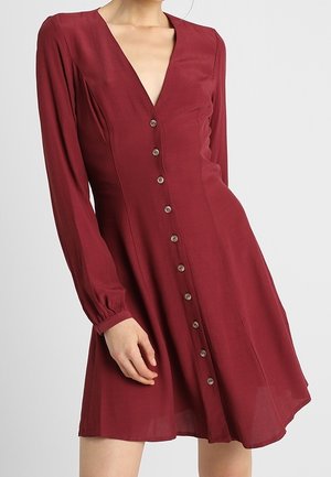 Bordeaux lange mouw jurk met een V-halslijn, knoopsluiting aan de voorkant en een getailleerd lijfje, uitlopend in een A-lijn rok. Zachte stof met een gladde textuur.