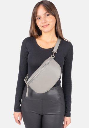 Sac bandoulière en cuir gris à texture lisse, forme arrondie et fermeture éclair. Porté sur l'épaule avec un haut noir.