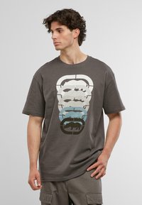 Grå bomulds-T-shirt med et grafisk motiv af stablede dyresilhuetter i hvid, lys grå, blå og sort. Korte ærmer og rund halsudskæring.
