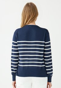 Granatowy sweter z pionowymi białymi paskami, długimi rękawami i ściągaczem. Wykonany z miękkiego materiału, luźny krój i okrągły dekolt.