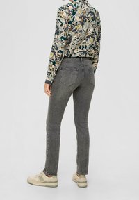 Jeans in denim grigio con un design aderente, cinque tasche e vita a media altezza. Abbinati a un top a maniche lunghe a fantasia e sneakers beige.