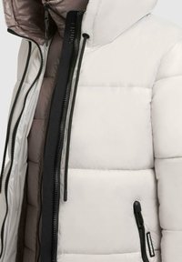 Chaqueta acolchada ligera con capucha, hecha de material blanco brillante. Presenta cierre con cremallera, cordones ajustables y bolsillos laterales.